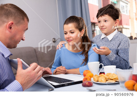 Happy ordinary couple with teenager son using laptop during breakfast at home 90560976