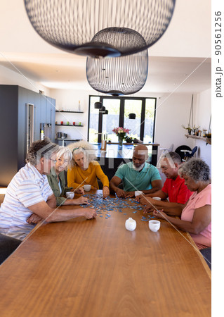 Senior multiracial friends playing jigsaw puzzle on wooden table while sitting in retirement home 90561256
