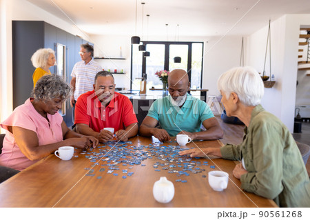 Multiracial senior friends solving jigsaw puzzle on wooden table while sitting in nursing home Multiracial senior friends solving jigsaw puzzle on wooden table while sitting in nursing home 90561268