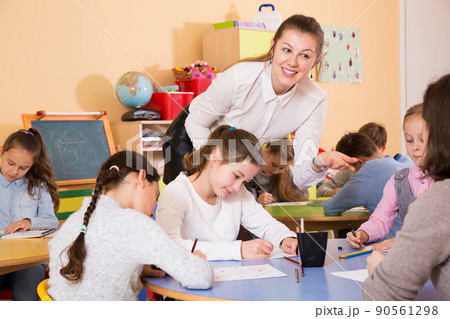 boys and girls sitting and teacher helping drawing 90561298