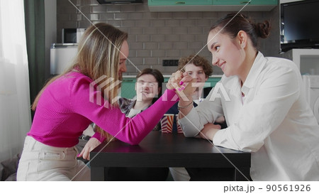 A group of friends are playing arm wrestling. Girls fight with their hands on the table A group of friends are playing arm wrestling. Girls fight with their hands on the table 90561926
