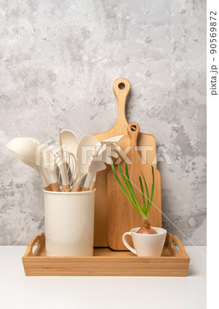 Cooking utensil set on kitchen table aga. Silicone kitchen tools, wooden cutting boards on a tray. Front view Cooking utensil set on kitchen table aga. Silicone kitchen tools, wooden cutting boards on a tray. Front view 90569872