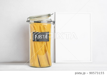 Organization of storage in the kitchen. Pasta in glass container on a kitchen table. White empty frame for text. Zero waste storage Organization of storage in the kitchen. Pasta in glass container on a kitchen table. White empty frame for text. Zero waste storage 90573155