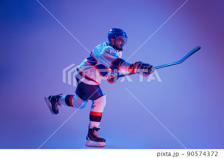 In action. Professional hockey player in sports uniform and protective equipment skating isolated on purple background. Concept of sport, active lifestyle, motion, movement, ad. 90574372