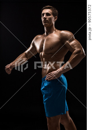 Muscular and fit young bodybuilder fitness male model posing over black background. 90575372