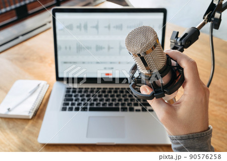 Man's hand holding a microphone on home studio podcast background 90576258