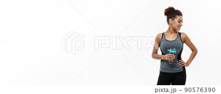 Healthy and Fitness concept - beautiful African American girl in sport clothes holding water bottle after workout. Isolated on white studio background Healthy and Fitness concept - beautiful African American girl in sport clothes holding water bottle after workout. Isolated on white studio background 90576390