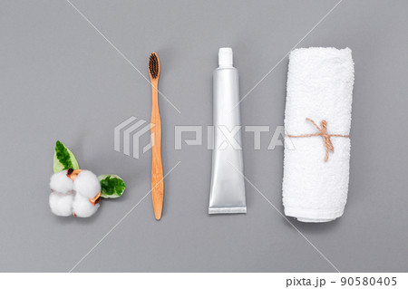 Healthcare and beaty. A roll of white towel, toothpaste, a bamboo toothbrush, and a cotton flower. Flat lay. Gray background. The concept of eco-friendly hygiene products 90580405