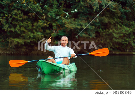 Kayaking on the river. Adult man is sitting in a kayak and gives a thumbs up. Copy space. The concept of the World Tourism Day Kayaking on the river. Adult man is sitting in a kayak and gives a thumbs up. Copy space. The concept of the World Tourism Day 90580849