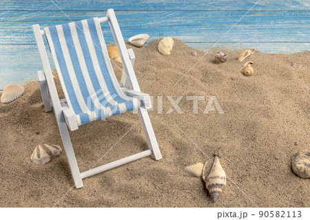 Sun lounger and seashells on the sand on a blue background Sun lounger and seashells on the sand on a blue background 90582113