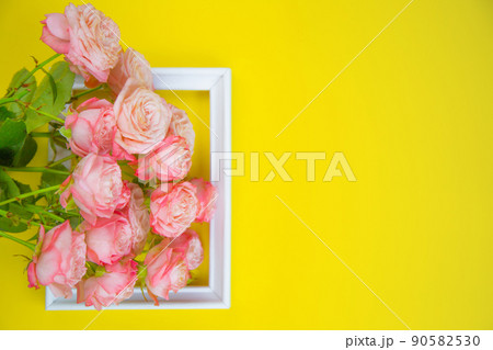 A large bouquet of pink roses lies on top of a small frame on a bright yellow background with a place for text. High quality photo 90582530