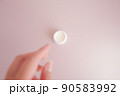 ピンクの背景に置かれた白い容器に入ったクリームを手に取ろうとしてる女性の手元の写真素材 90583992