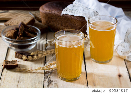 Traditional Russian cold rye drink Kvas in a glass and a jug on a wooden table. Kvass from bread, rye malt, sugar and water. Traditional Russian cold rye drink Kvas in a glass and a jug on a wooden table. Kvass from bread, rye malt, sugar and water. 90584317