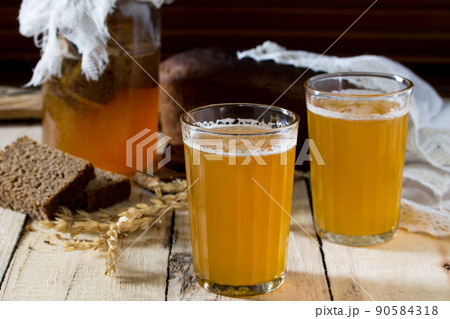 Traditional Russian cold rye drink Kvas in a glass and a jug on a wooden table. Kvass from bread, rye malt, sugar and water. Traditional Russian cold rye drink Kvas in a glass and a jug on a wooden table. Kvass from bread, rye malt, sugar and water. 90584318