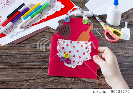 Creates a baby gift from a paper apron postcard for grandmother on mother's day. Hand-made. The project of children's creativity, needlework, crafts for children. Creates a baby gift from a paper apron postcard for grandmother on mother's day. Hand-made. The project of children's creativity, needlework, crafts for children. 90585176