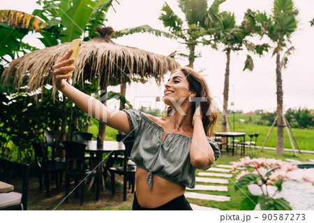Happy young woman taking selfie on smartphone in exotic garden Happy young woman taking selfie on smartphone in exotic garden 90587273