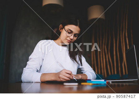 Thoughtful female freelancer working with documents while sitting at table with laptop 90587417