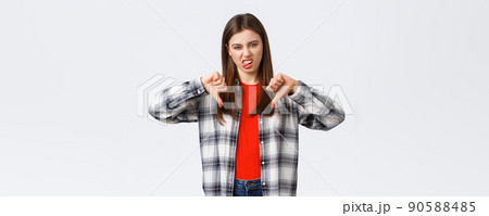 Lifestyle, different emotions, leisure activities concept. Displeased and unimpressed young picky girl in checked shirt, thumb-down and show tongue to express dislike, rate awful movie Lifestyle, different emotions, leisure activities concept. Displeased and unimpressed young picky girl in checked shirt, thumb-down and show tongue to express dislike, rate awful movie 90588485
