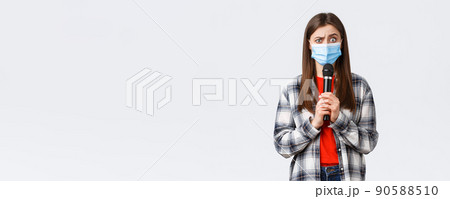Coronavirus outbreak, leisure on quarantine, social distancing and emotions concept. Confused woman in medical mask look smth strange, holding microphone, perform, white background 90588510