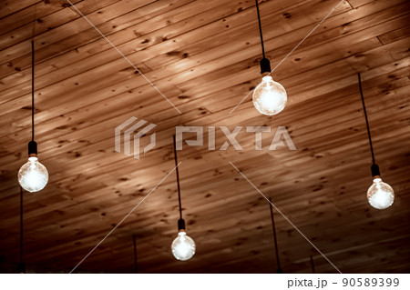 Old incandescent lamps hang on wires on a wooden ceiling. Retro design. 90589399