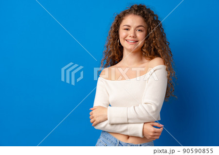 Portrait of a young attractive curly-haired woman against blue background Portrait of a young attractive curly-haired woman against blue background 90590855