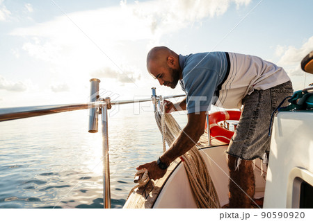 Young african american sailor tying ropes on sailboat in the sea on sunset 90590920