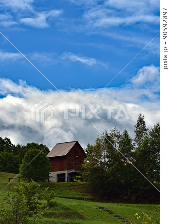 青い空、白い雲、樹木の緑に囲まれた2階建て赤い屋根のコテージです。 90592897