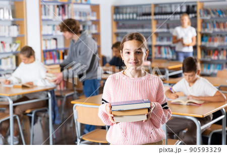 Preteen girl standing with a stack of books inlibrary 90593329