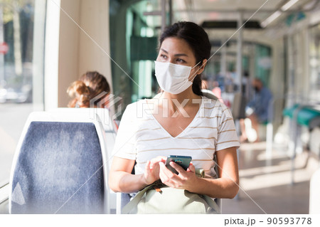 Woman in mask with smartphone sitting in tram Woman in mask with smartphone sitting in tram 90593778