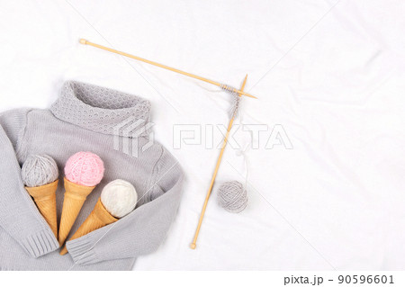 Gray knitted sweater, wooden knitting needles and ice cream cones with yarn on white background. Knitting, hobby and handmade creative concept. Top view Flat lay Copy space 90596601