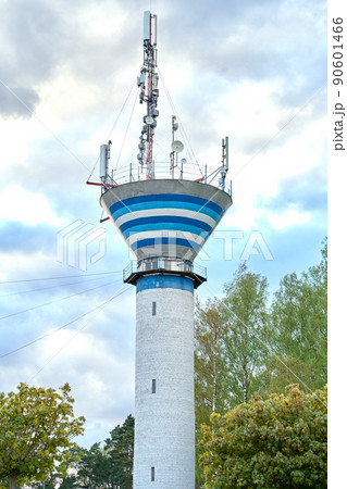 White brick water tower with wireless communication antenna transmitter against blue sky and trees.Internet, 3G, 4G and 5G cellular connection. 90601466