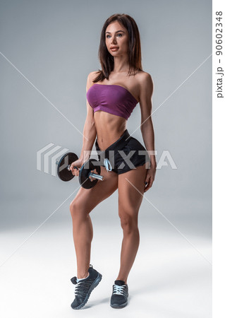 Studio portrait of a sporty young woman posing with dumbbell against a gray background Studio portrait of a sporty young woman posing with dumbbell against a gray background 90602348