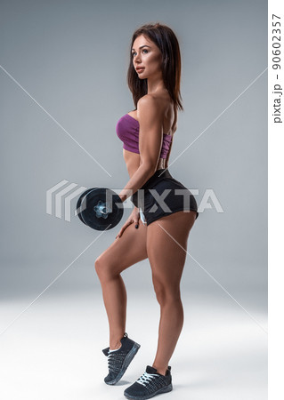 Studio portrait of a sporty young woman posing with dumbbell against a gray background 90602357