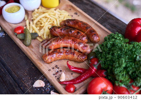 Tasty freshly grilled Sausages served with French fries and sauce on wooden board 90603412