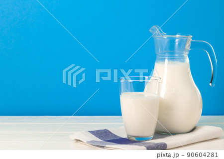 Glass and pitcher of milk against blue background Glass and pitcher of milk against blue background 90604281