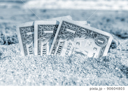 Three paper cash one dollar bills half buried in the sand on the seashore close-up. Concept money, business, savings, financial, investment, cash. Blue color 90604803