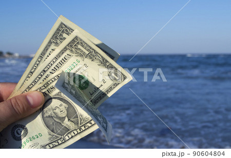 Person holds in his hand three dollar bills on the background of the waves of the blue sea. Concept money finance business tourism travel, money spending, cash expenses. Money cash expenses business 90604804
