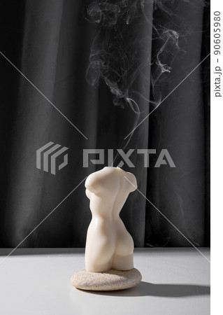 Candle in woman torso shape burning in grey interior in slow motion, atmosphere and smoke after candle 90605980