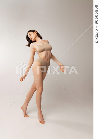 Portrait of beautiful young woman posing in beige underwear isolated over grey studio background. Natural beauty 90606809