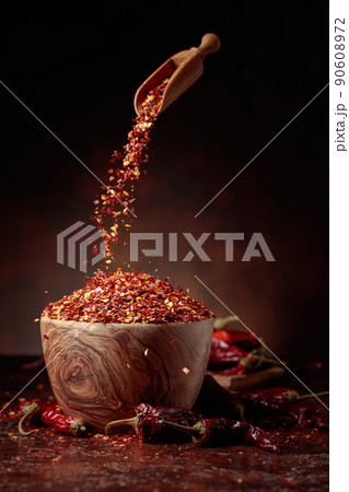 Chilli flakes are poured into a wooden dish. 90608972