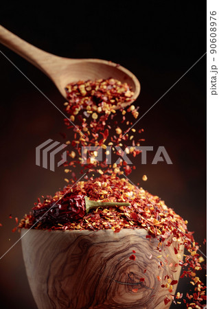 Chilli flakes are poured into a wooden dish. 90608976