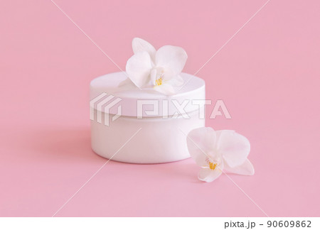White cream jar near white orchid flowers on light pink close up. Mockup. Skincare product 90609862