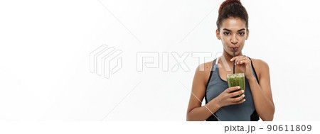 Healthy and Fitness concept - Beautiful American African lady in fitness clothing drinking healthy vegetable drink. Isolated on white background. Healthy and Fitness concept - Beautiful American African lady in fitness clothing drinking healthy vegetable drink. Isolated on white background. 90611809