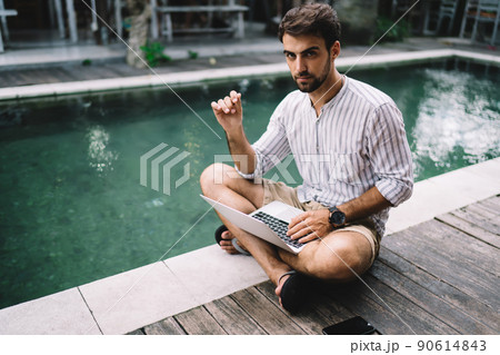 Serious businessman with laptop in casual summer wear on poolside 90614843