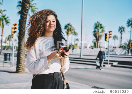 Happy curly blogger with cellphone for online networking posing at sunny street Happy curly blogger with cellphone for online networking posing at sunny street 90615089