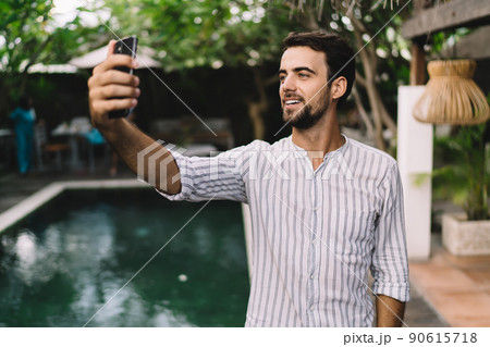 Cheerful young man taking self portrait on smartphone during summer holidays Cheerful young man taking self portrait on smartphone during summer holidays 90615718