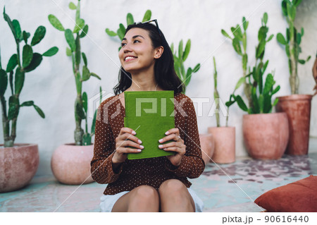 Smiling young Asian woman enjoying interesting book on veranda Smiling young Asian woman enjoying interesting book on veranda 90616440