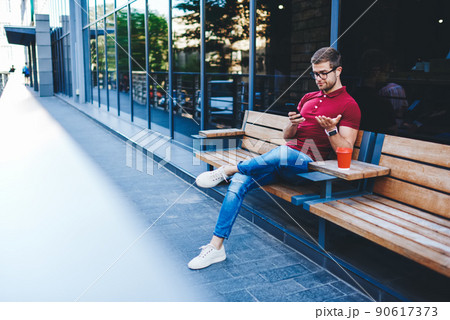 Unsatisfied guy reading news on smartphone while sitting outdoors Unsatisfied guy reading news on smartphone while sitting outdoors 90617373