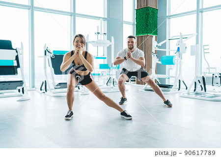 Cheerful sportspeople doing side lunges Cheerful sportspeople doing side lunges 90617789