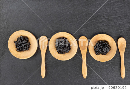 Wooden mini plates with black caviar on a stone board for serving and wooden mini spoons. Wooden mini plates with black caviar on a stone board for serving and wooden mini spoons. 90620192